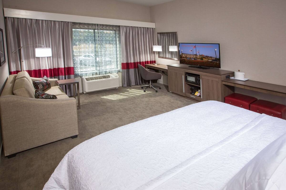 A hotel room with a bed, a desk, a chair, a television, and a window with curtains.