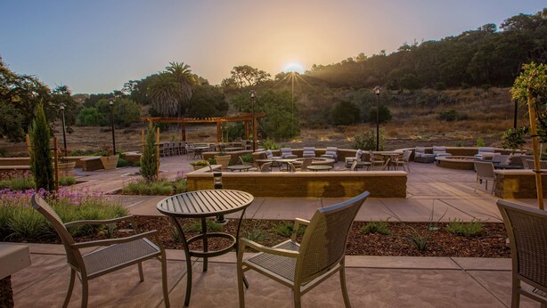 An outdoor patio area with multiple seating arrangements, including round tables and chairs, and a pergola structure.