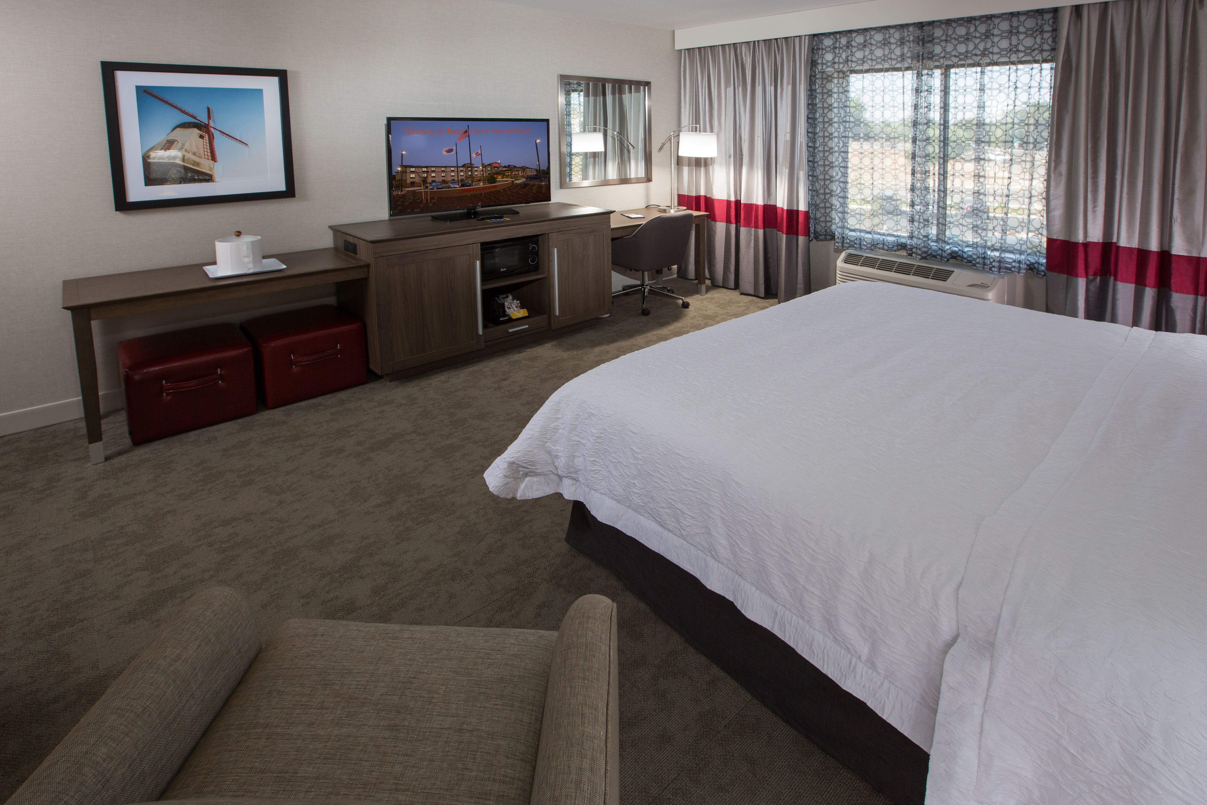 A hotel room with a large bed, a desk with a computer, a television, and a window with curtains.