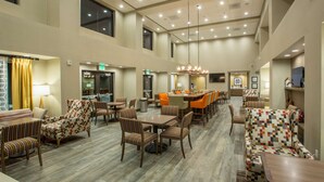 A spacious hotel lobby with multiple seating areas, a central dining table, and a chandelier.