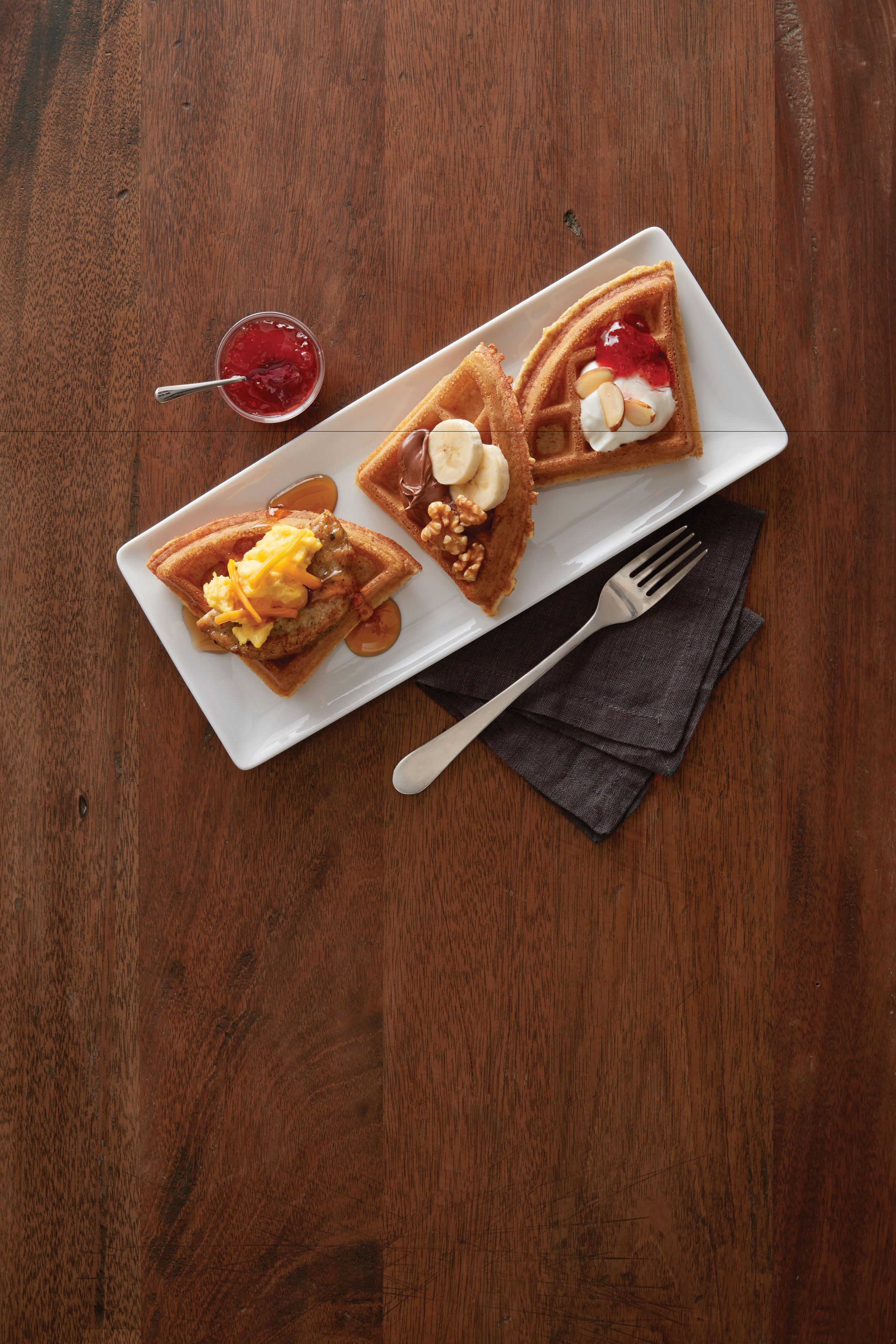 Une assiette de gaufres garnies et un petit bol de confiture sur une table en bois.