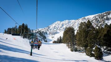 A ski lift chair ascending a snowy mountain slope with a clear blue sky.