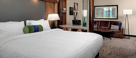 Une chambre d’hôtel avec un grand lit, un bureau, un canapé en cuir et un tableau encadré au mur.