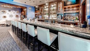 Uma área de bar com um balcão comprido, vários bancos altos e uma variedade de garrafas e copos.