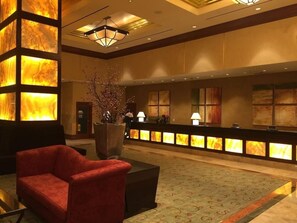 A lobby with a reception desk, a red armchair, a large vase with branches, and a patterned carpet. - Fallon Luxury Rentals at The Signature (Las Vegas)