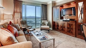 Quarto de hotel com uma janela grande, um sofá, uma mesa de centro, uma televisão e um armário de madeira.