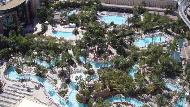 Vista aérea de um hotel com várias piscinas, cercado por palmeiras e áreas de lazer.