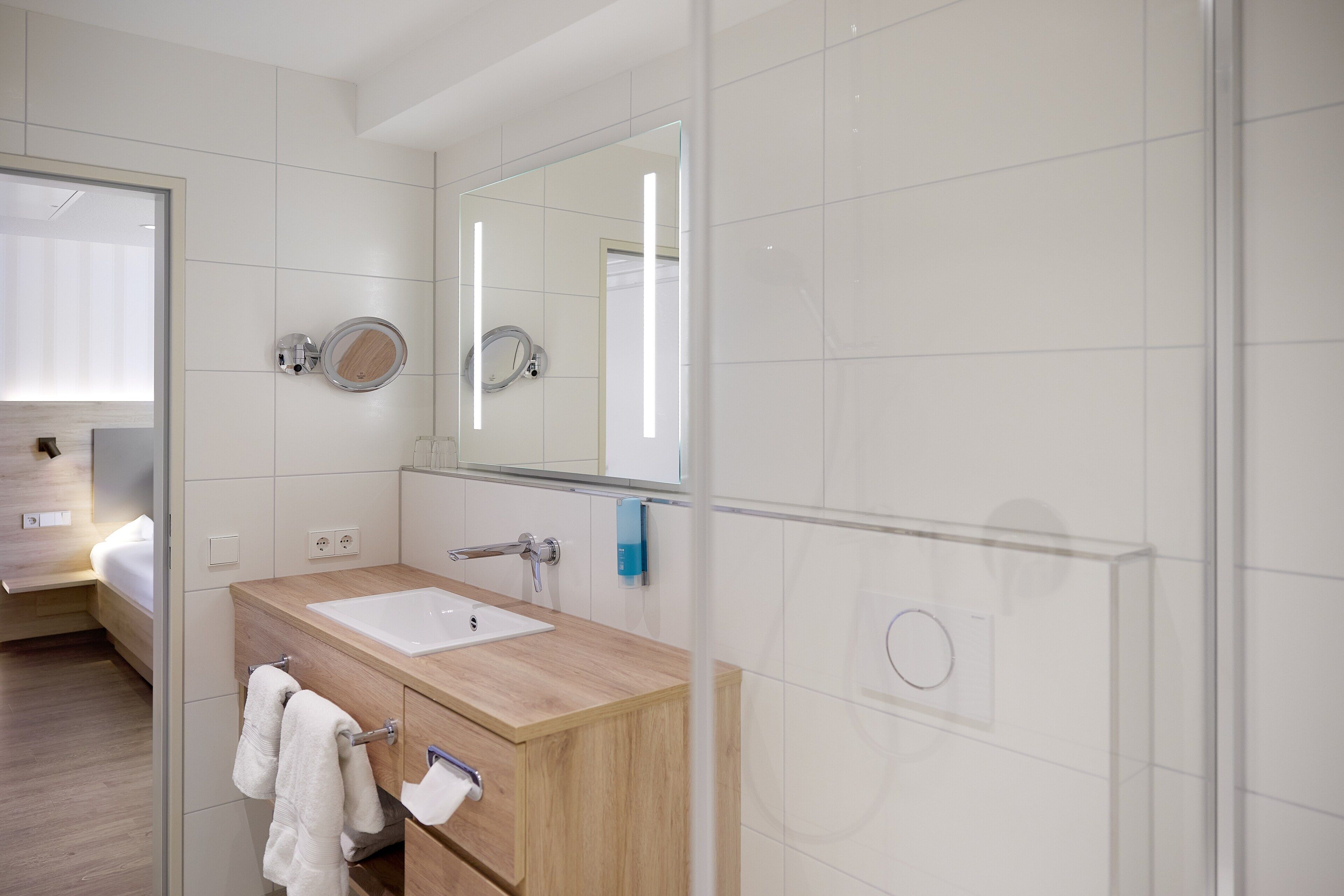 A modern bathroom with a wooden vanity, a large mirror, and a built-in sink.