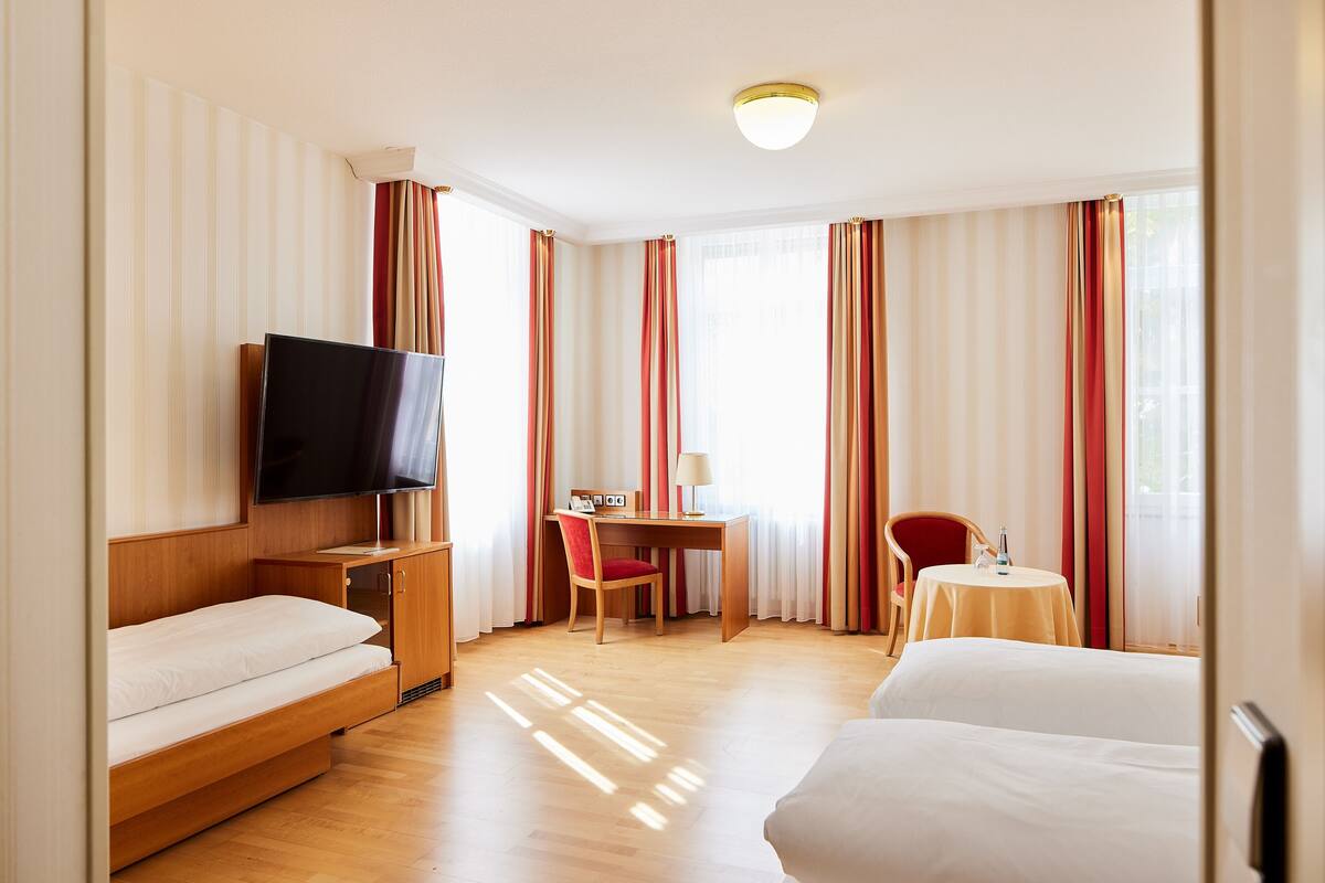 Habitación de hotel con cama, escritorio y silla, televisor y una pequeña mesa con otra silla.