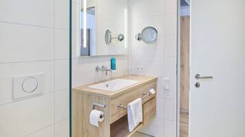 A modern bathroom with a wooden vanity, a large mirror, a sink, and a glass shower enclosure.