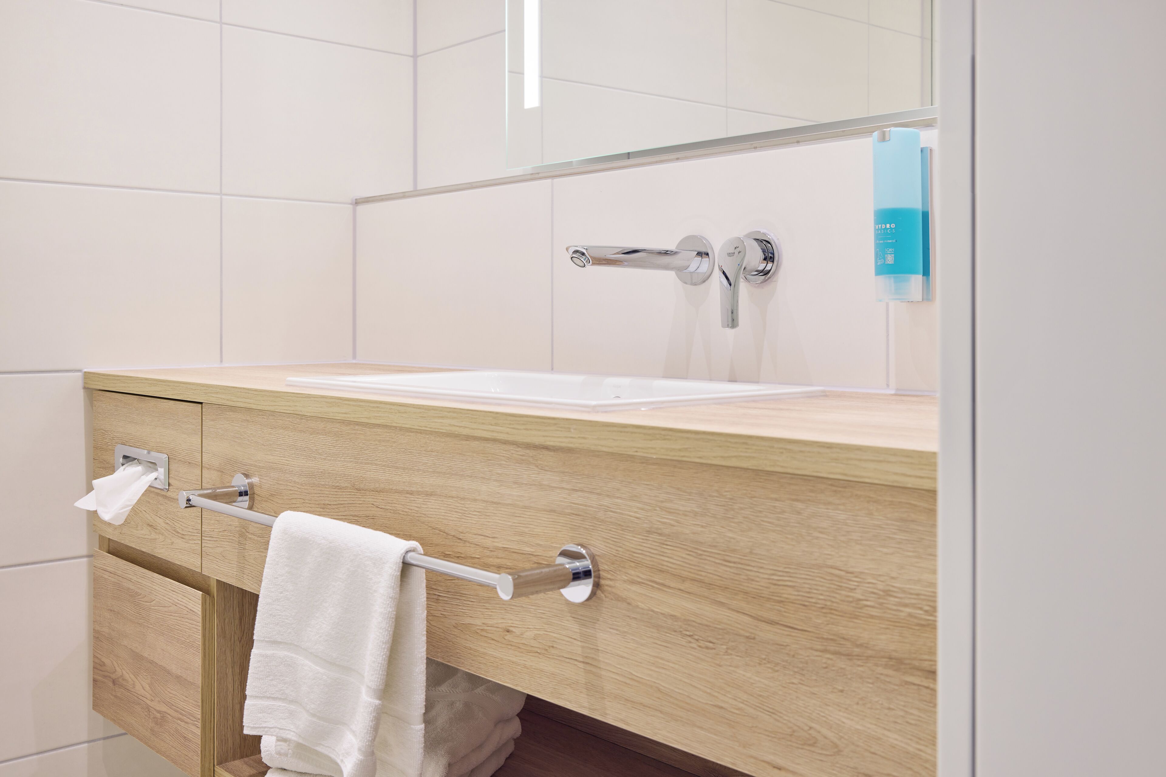 A modern bathroom with a wooden vanity, a white sink, and a towel rack.