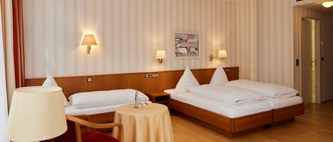 A hotel room with two single beds, a small table, a chair, and two wall-mounted lamps.