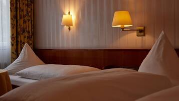 Een hotelkamer met twee bedden, elk voorzien van witte lakens en kussens, en twee wandlampen.