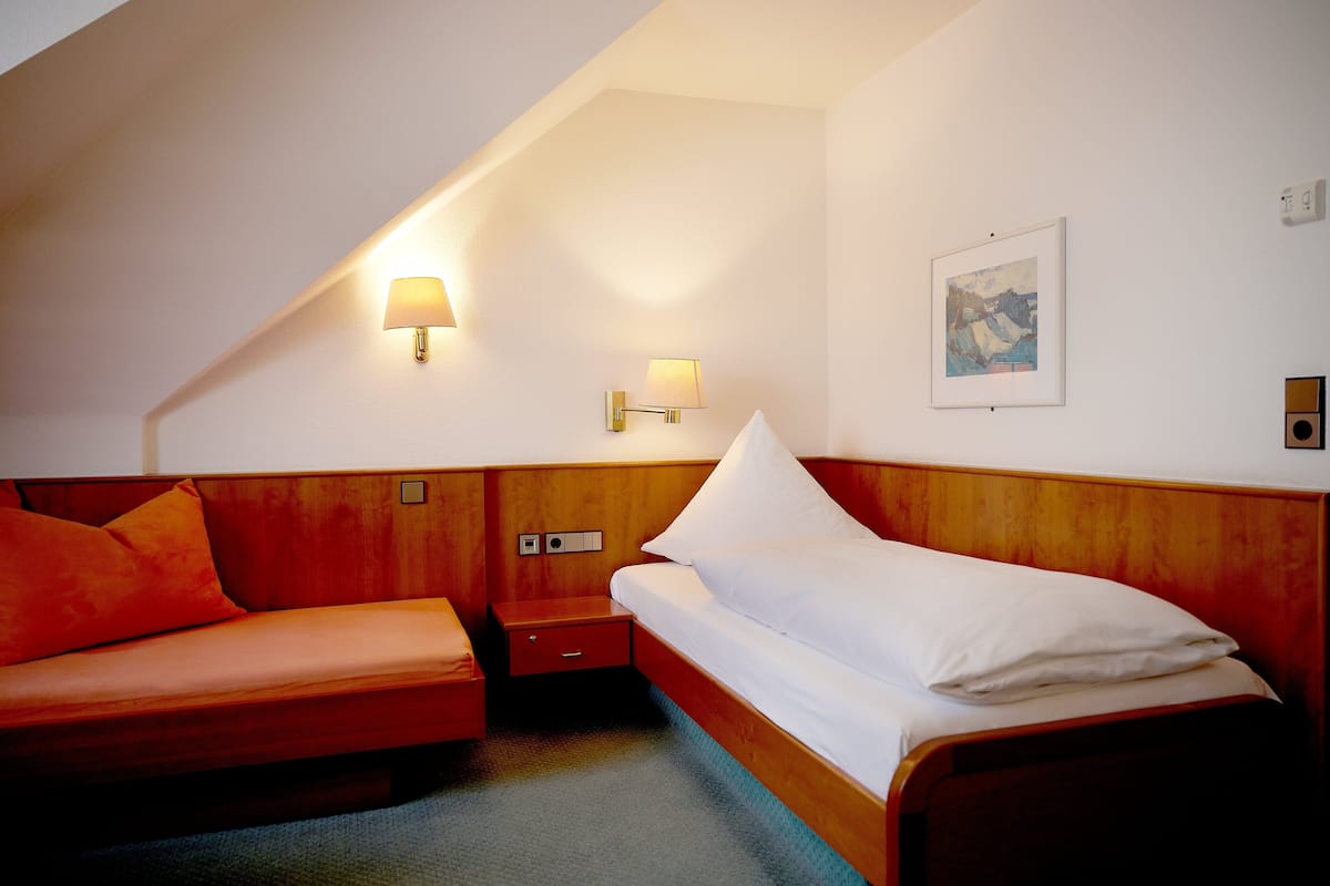 Habitación de hotel con cabecera de madera, una cama individual, mesita de noche de madera, una lámpara y un cuadro en la pared.