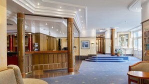 A hotel lobby with a reception desk, seating area, and a staircase leading to an upper floor.