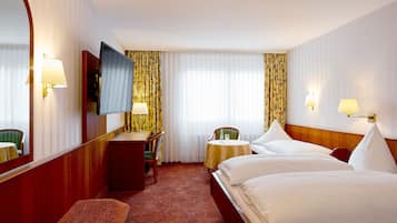 A hotel room with a large bed, a desk, a chair, a small table, and a TV.