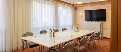 Ein Konferenzraum mit einem langen Tisch, Stühlen, einem Flachbildfernseher und einer Whiteboard-Tafel.