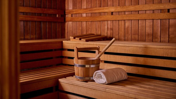 A wooden sauna with benches, a wooden bucket, and a rolled-up towel.