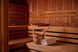 Un sauna en bois avec des bancs, un seau en bois et une serviette enroulée.