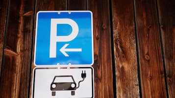Señal de estacionamiento con una flecha direccional y un símbolo de vehículo eléctrico.