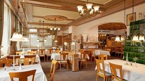 A restaurant with multiple tables, wooden chairs, and hanging chandeliers.
