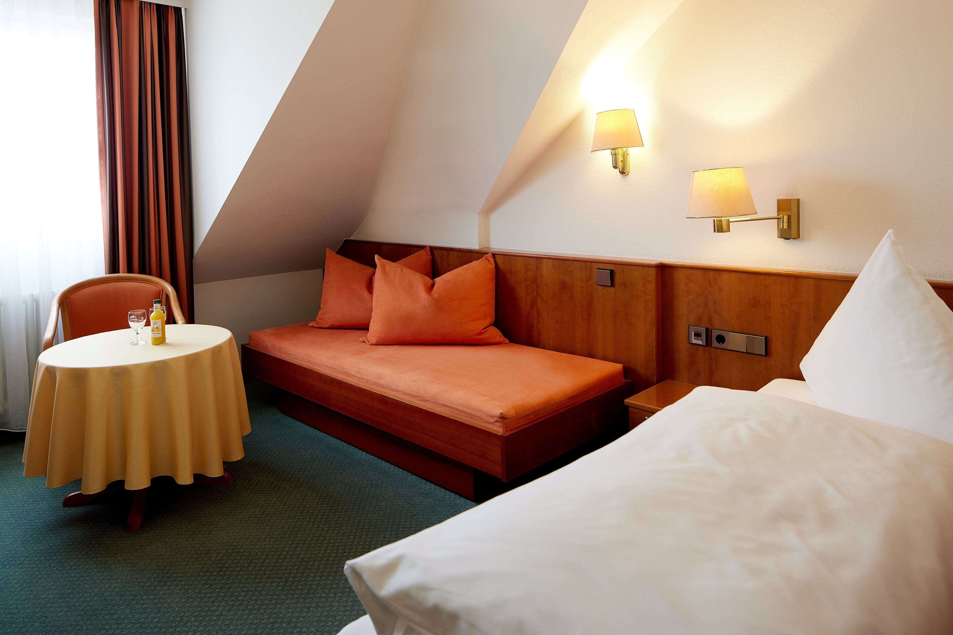 Une chambre d’hôtel avec un lit, une petite table sur laquelle se trouvent une bouteille et un verre, et une chaise.