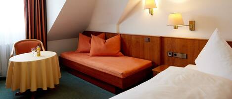 Une chambre d’hôtel avec un lit, une petite table sur laquelle se trouvent une bouteille et un verre, et une chaise.