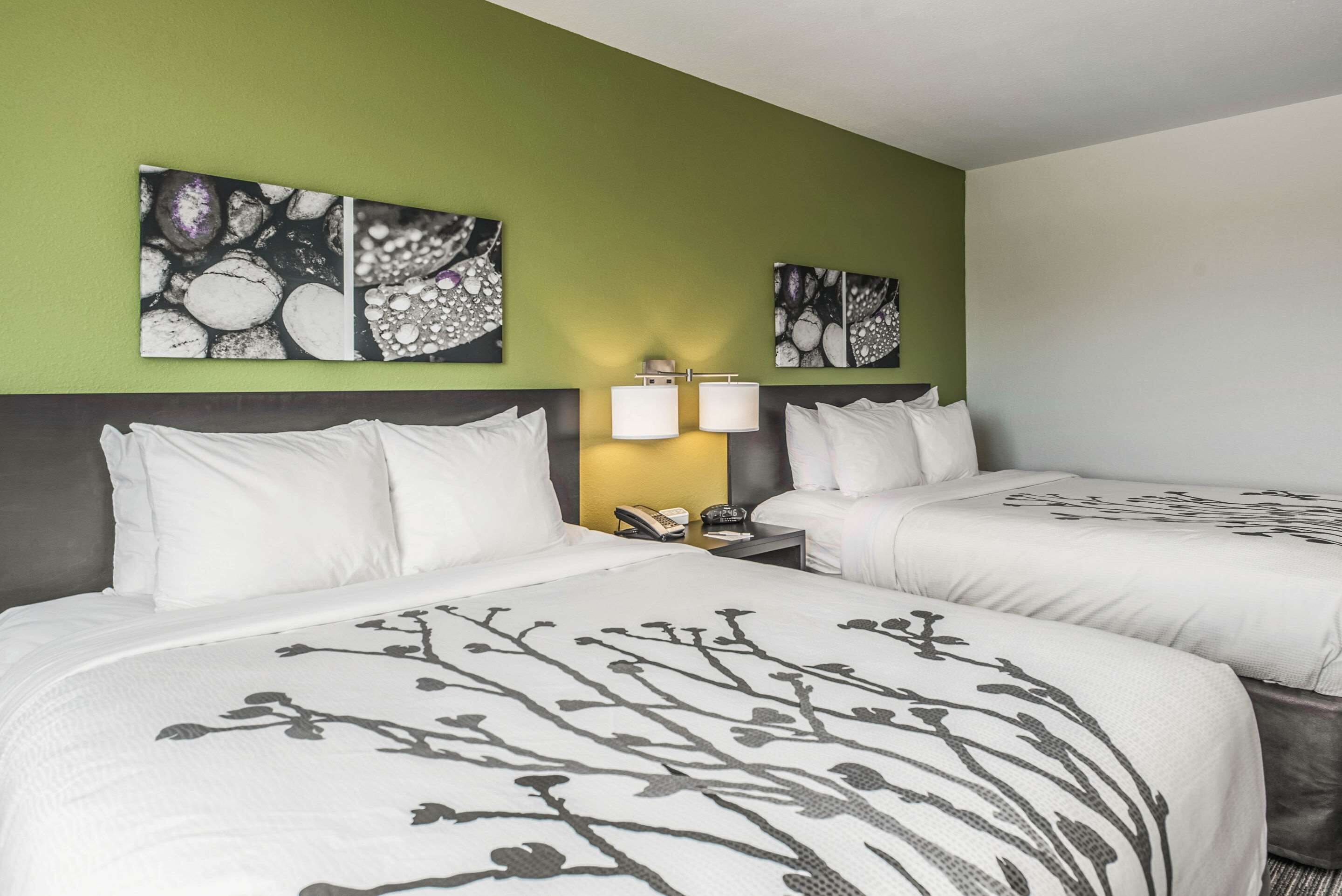 A hotel room with two beds, green walls, and artwork above the beds.