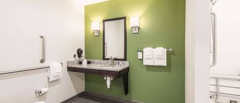 A bathroom with a green wall, a sink with a marble countertop, a toilet, and a shower area.