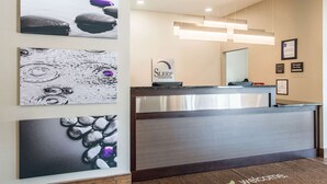 Uma área de recepção de hotel com design moderno, apresentando um balcão de recepção, uma placa com a inscrição 'Sleep In Suites' e três obras de arte emolduradas na parede.