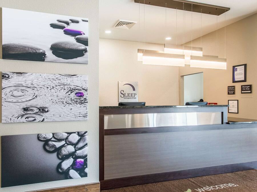 A hotel reception area with a modern design, featuring a reception desk, a 'Sleep In Suites' sign, and three framed artworks on the wall.