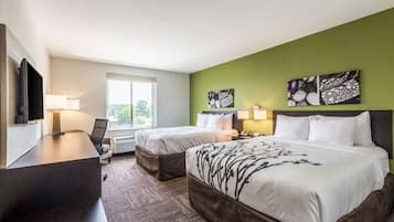 A hotel room with two beds, a desk, a TV, and artwork on the walls.