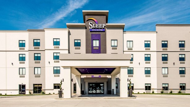 Edifício Sleep Inn & Suites com design moderno, destacando uma entrada imponente e um céu claro acima.