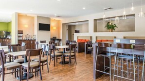 Um restaurante moderno com mesas e cadeiras de madeira, um espaço de bar e uma televisão na parede.