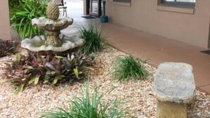 A building entrance with a stone fountain, potted plants, and a gravel pathway. - Dinner Bell Motel (Dunnellon)