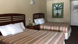 A hotel room with two beds, each with striped bedding, a nightstand with a lamp, a painting on the wall, and a ceiling fan. - Dinner Bell Motel (Dunnellon)