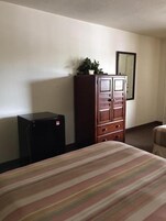 A hotel room with a bed, a wooden dresser, a black cabinet, and a mirror on the wall.