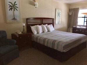 A hotel room with a bed, a nightstand, a lamp, a chair, and a window with curtains. - Dinner Bell Motel (Dunnellon)