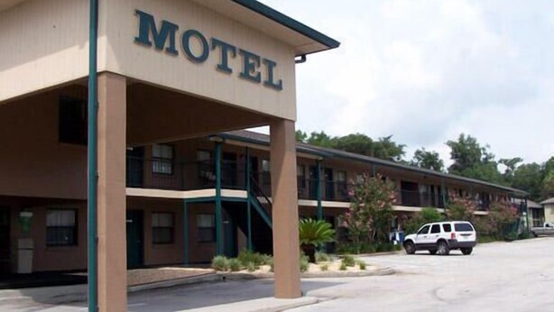 A motel with a prominent 'MOTEL' sign, a covered parking area, and a row of rooms with balconies. - Dinner Bell Motel (Dunnellon)