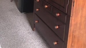 A dark wooden wardrobe with multiple drawers and a mirrored door, situated in a room with a carpeted floor and a plant in the background. - Dinner Bell Motel (Dunnellon)
