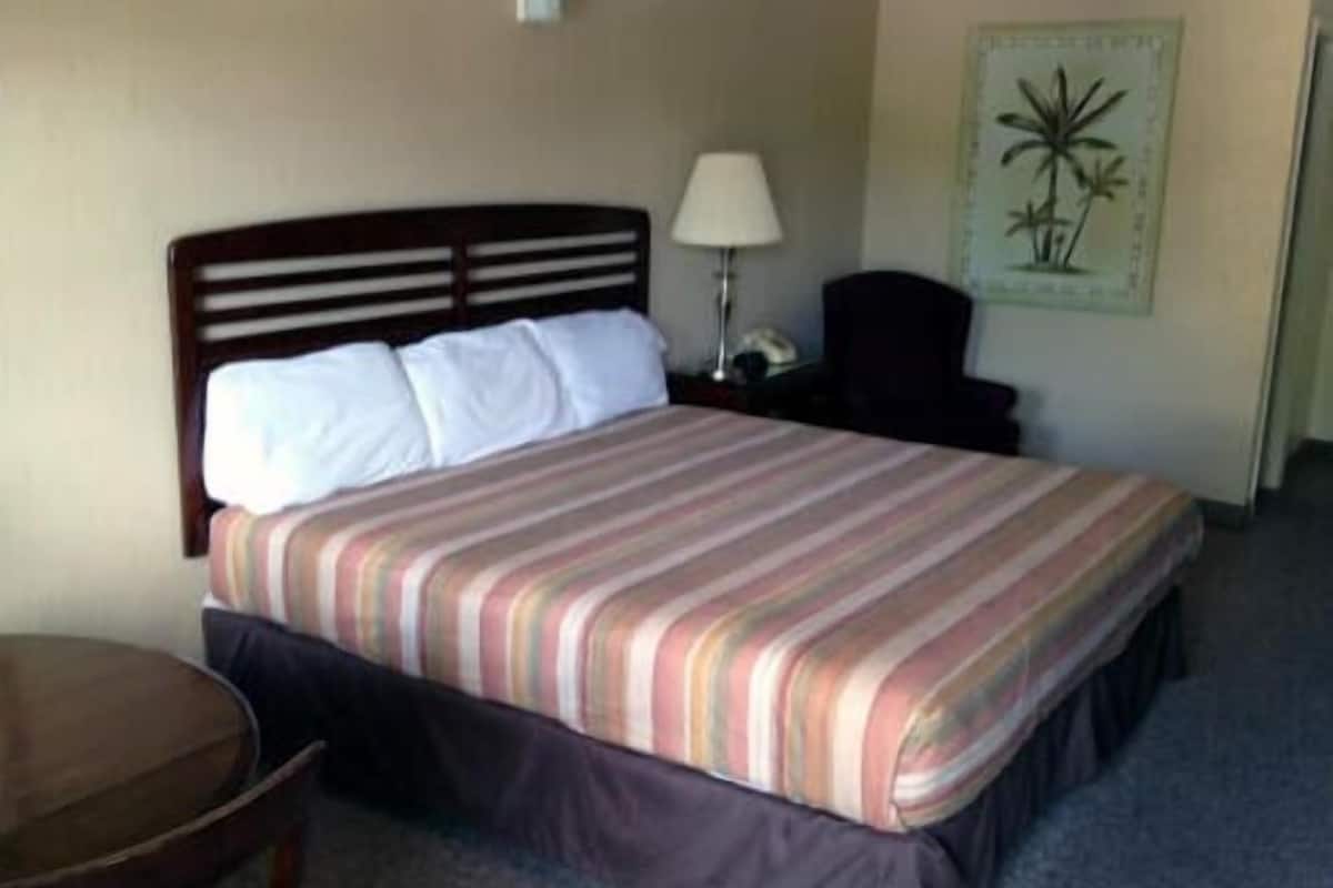A hotel room with a bed, a nightstand, a lamp, a chair, and a small table.