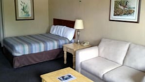 A hotel room with a bed, a sofa, a small table, and two framed pictures on the wall. - Dinner Bell Motel (Dunnellon)