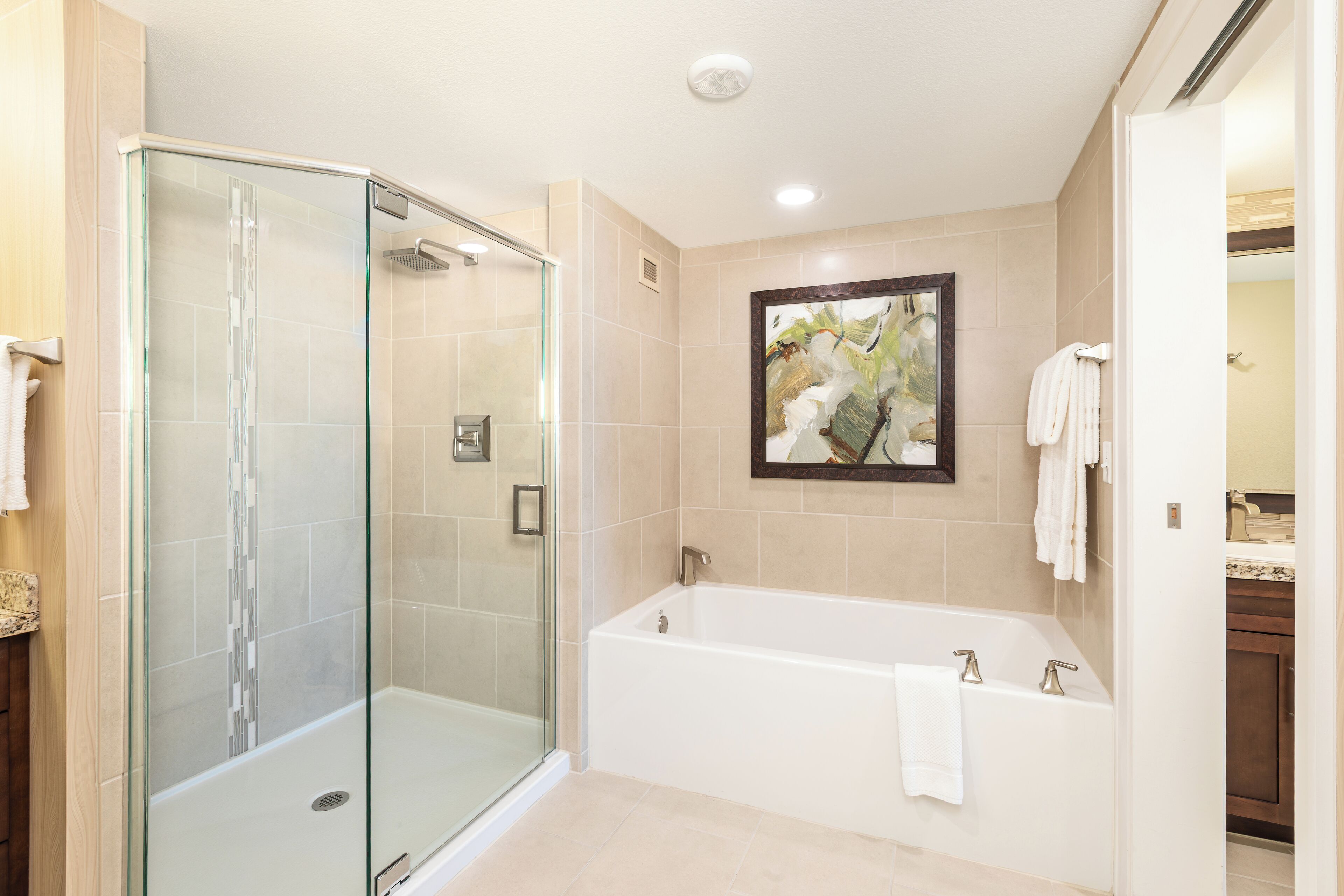 A modern bathroom with a glass-enclosed shower, a freestanding bathtub, and a framed artwork on the wall.