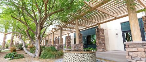 A covered outdoor area with a stone fountain, wooden pergola, and stone pillars.