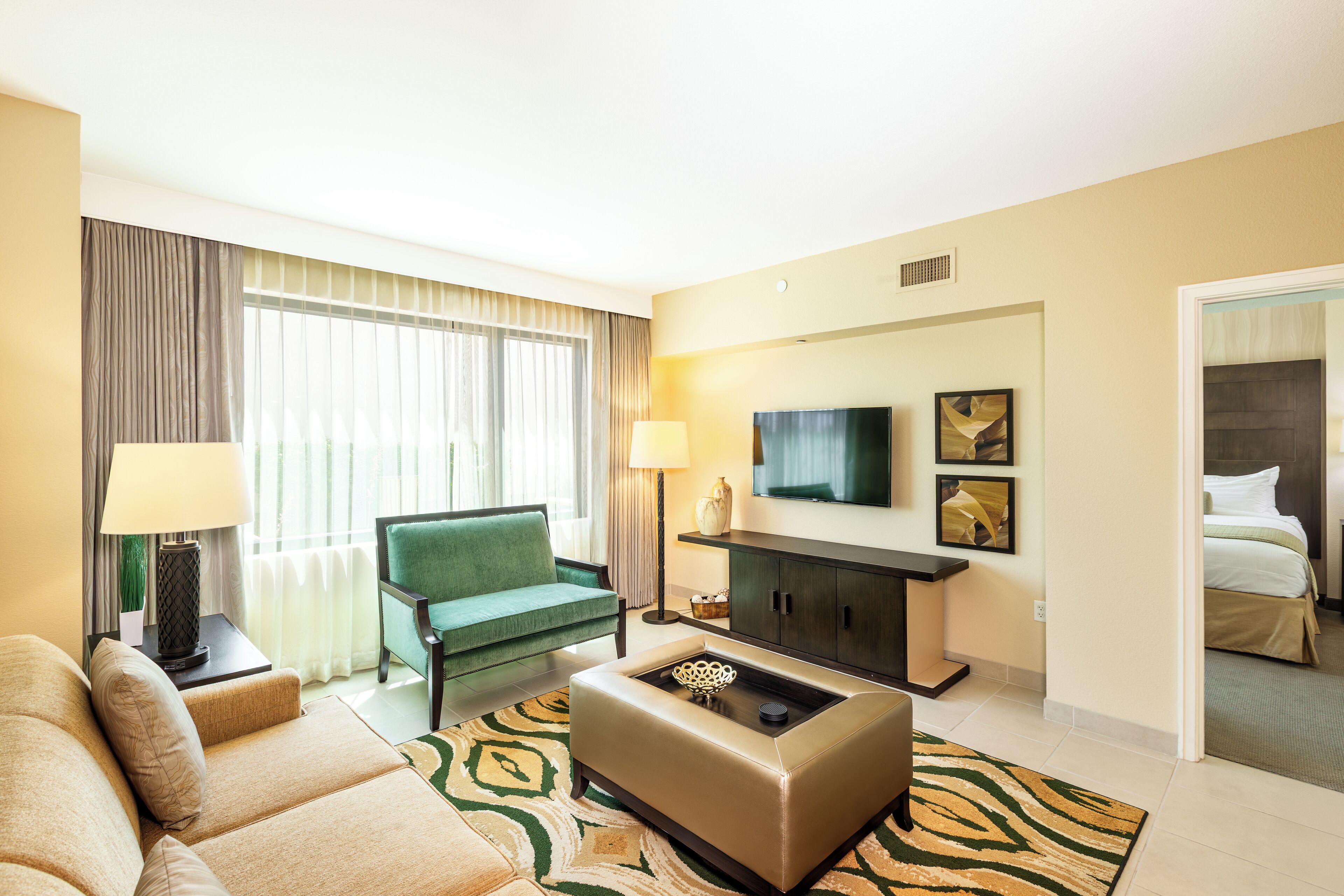 A hotel room with a sofa, a green armchair, a coffee table, a TV, and a bed.