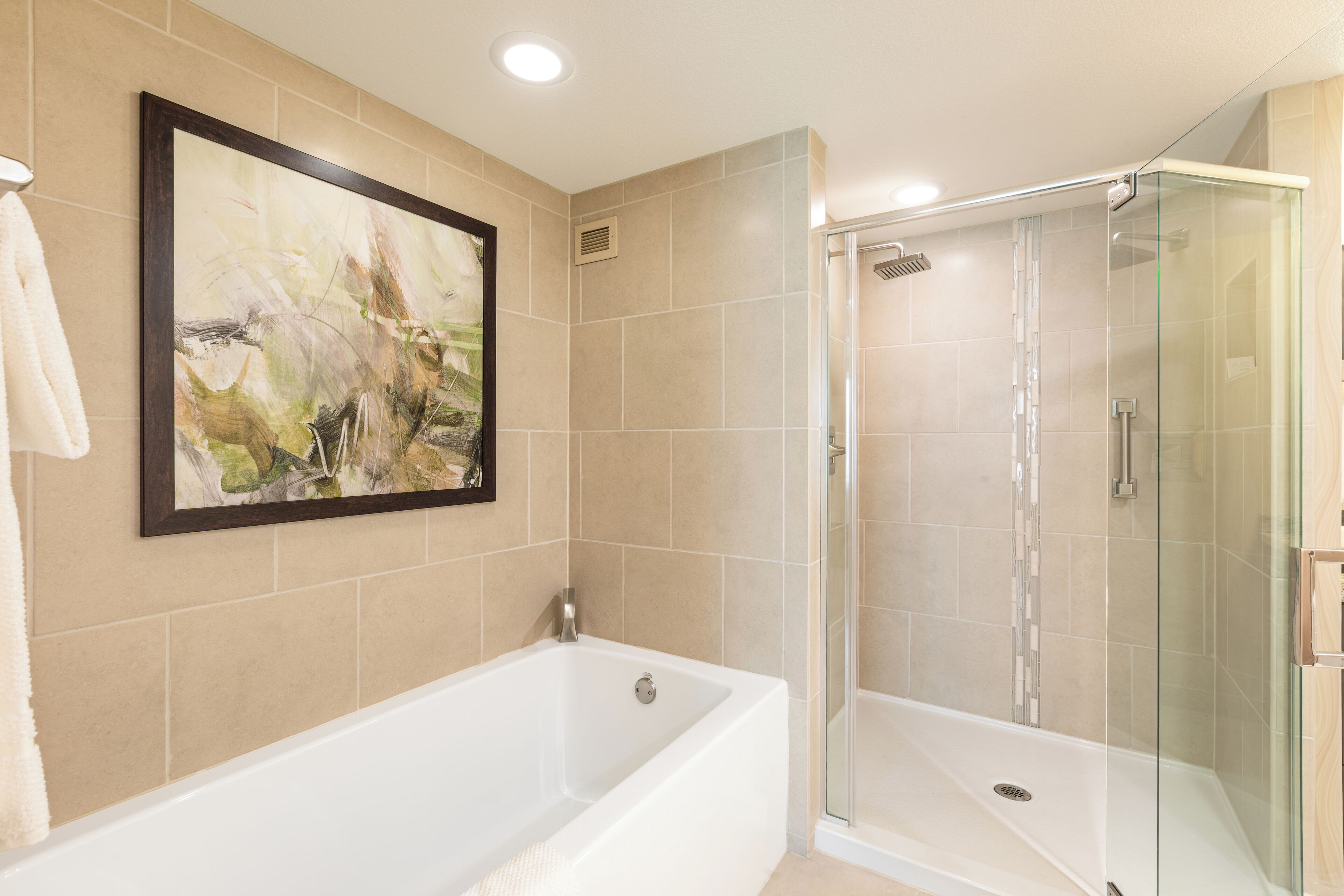 A modern bathroom with a bathtub, a glass shower enclosure, and a framed abstract painting on the wall.