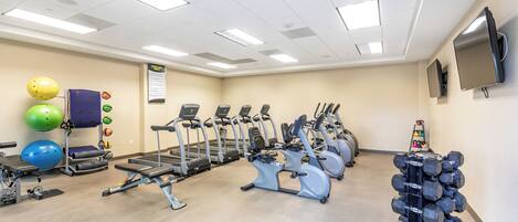 A gym with treadmills, elliptical machines, and a rack of dumbbells.