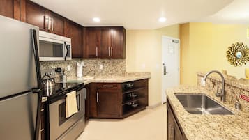 Una cocina con armarios de madera oscura, un lavamanos de acero inoxidable, encimeras de granito y microondas integrado.
