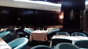 A dining area with tables and chairs, some with tablecloths, and a dark wall with a logo.