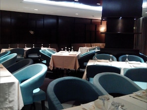 Un espace repas avec des tables et des chaises, dont certaines sont recouvertes de nappes, et un mur sombre orné d’un logo.